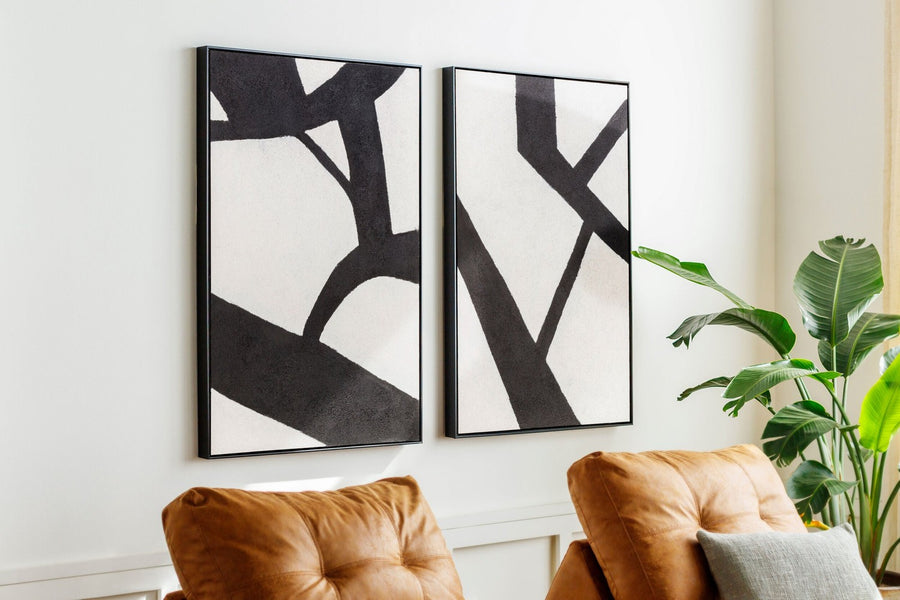 Pair of black and white hand-painted canvases hung above a cognac leather sofa