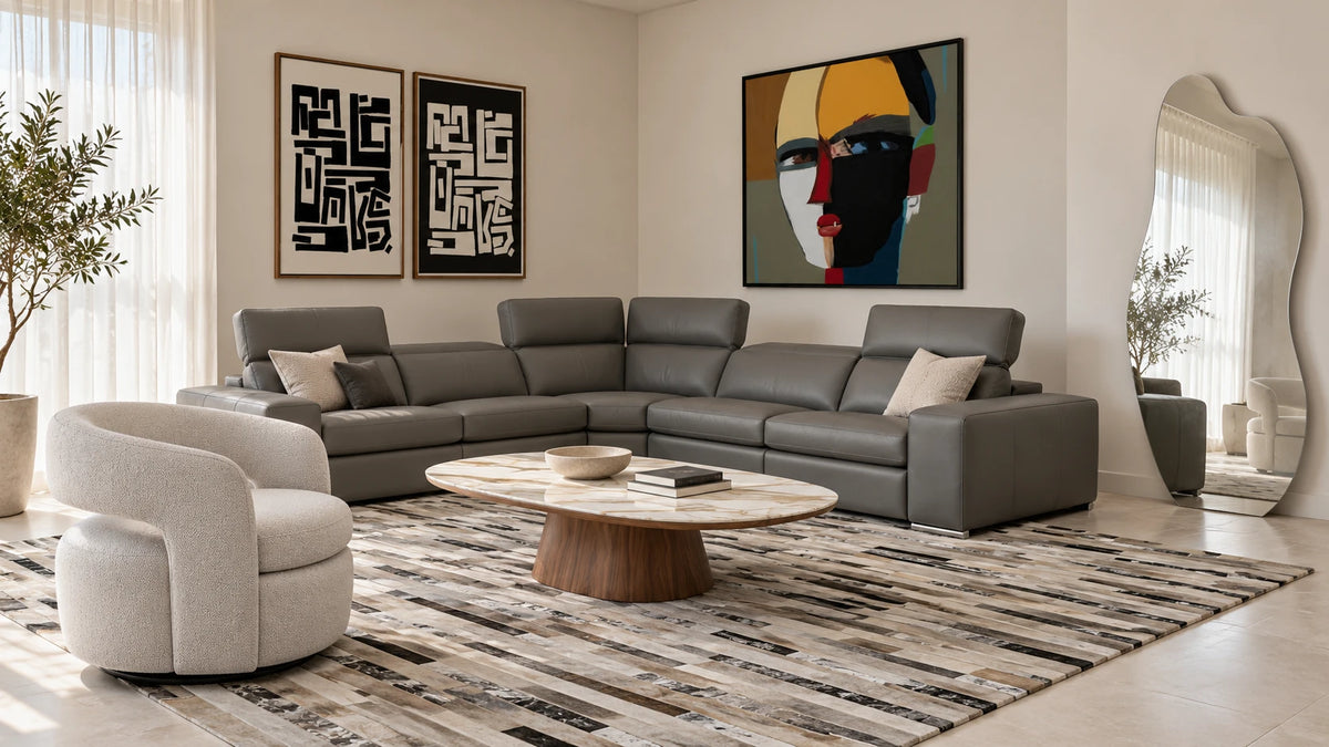 Living room with a gray leather corner sectional, an oval marble-top walnut coffee table, a textured swivel chair, a striped cowhide rug and bold modern art